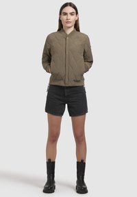 Gequilted olijfgroene bomberjack met een ritssluiting, geribde manchetten en zoom; gecombineerd met zwarte denim shorts en zwarte enkellaarsjes.