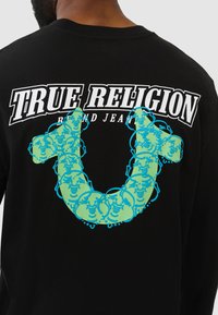Schwarzes Langarm-T-Shirt mit dem "TRUE RELIGION"-Logo in Weiß über einem türkisfarbenen und grünen stilisierten U-förmigen Design.