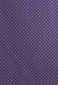 Tissu violet avec un motif géométrique répétitif composé de petits losanges bleus et noirs disposés en rangées diagonales.