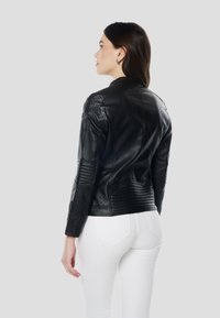 Čierna kožená bunda s prešívaným detailom na ramenách a rukávoch, s priliehavým strihom a vysokým golierom. Dokončenie zahŕňa tónované šitie.
