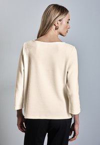 Top color crema con maniche a 3/4 in tessuto jacquard e scollatura a barca, caratterizzato da una vestibilità morbida e un design semplice.