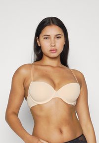 Nude push-up bra with smooth padded cups and thin adjustable straps, featuring a seamless design and delicate lace trim at the band.