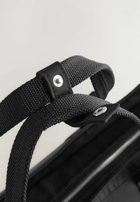 Schwarze Tragetasche aus strukturiertem Stoff, ausgestattet mit gewebten Griffen, silberfarbenen Hardware-Details und einem Reißverschlussfach.