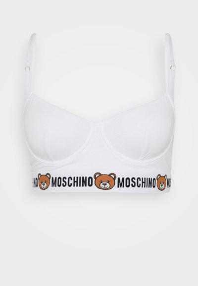 Bela bralette z gladko teksturo, ki ima grafiko risanega medveda in besedilo "Moschino" na elastiki na dnu.