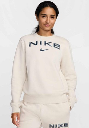 Bluzka Nike w kolorze ecru, z okrągłym dekoltem, ściągaczami przy mankietach oraz dużym granatowym logo na piersiach. Miękka w dotyku, luźny krój.