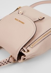 Sac à main en cuir rose avec ferrures dorées, comprenant une poche zippée, un rabat arrondi et une bandoulière réglable. Finition texturée avec une bordure contrastante.