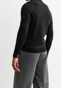 Pull noir ajusté avec un col rond, confectionné en matière lisse. Associé à un pantalon taille haute à carreaux gris.