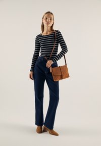Svart og hvitstripet langermet skjorte, blå høyt midje jeans, brun semsket håndveske og lysebrune ankelboots med hæl. Enkel design, uten mønstre.