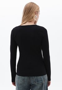 Schwarzes Langarmoberteil mit rundem Halsausschnitt, gefertigt aus glattem, elastischem Material. Das Design ist figurbetont und wird mit blauen Jeans kombiniert.