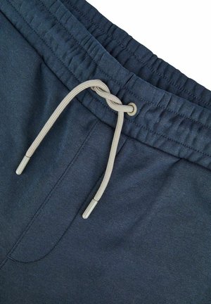 Marineblauwe joggingbroek met een elastische tailleband, voorzien van een trekkoord met beige accenten en metalen aglets. Glad katoenen stoftextuur.