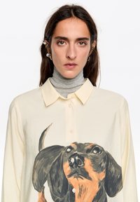 Camisa de manga larga en color crema con un gráfico pintado de un dachshund, cierre de botones en la parte delantera, tela suave y un corte relajado.