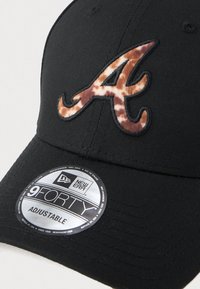 Czarna czapka z logo w kształcie litery 'A' w panterkę. Wykonana z materiału, ma regulowany pasek oraz okrągłą srebrną naszywkę z informacjami o marce.