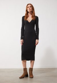 Robe noire à manches longues côtelées avec un décolleté en V profond, associée à des bottes à motif léopard brun, avec un talon épais.