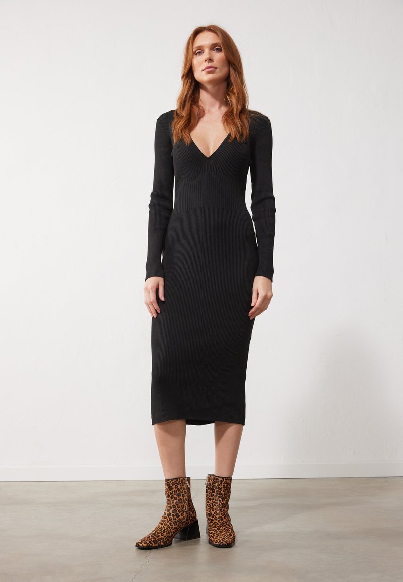 Robe noire à manches longues côtelées avec un décolleté en V profond, associée à des bottes à motif léopard brun, avec un talon épais.
