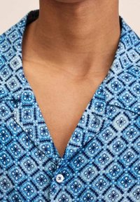 Korte mouwen shirt in blauw met een geometrisch patroon van diamanten en vierkanten. De stof is lichtgewicht met een zachte textuur. Knopsluiting zichtbaar.