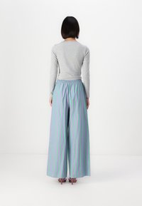Gray, ribbed long-sleeve top paired with wide, green and lavender striped trousers, featuring an elastic waistband and a flowing silhouette.