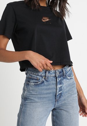 T-shirt noir court en coton, avec un logo Nike Air bronze sur la poitrine. Associé à un jean en denim bleu clair à taille haute.