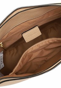Interno della borsa a tracolla in pelle color cuoio con una tasca con zip, foderato in tessuto liscio, e una leggera struttura a grana con un piccolo etichetta del marchio.