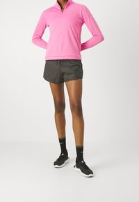 Růžová mikina na zip s dlouhým rukávem, černé lehké šortky, černé sportovní ponožky a boty s bílými akcenty. Jemné a prodyšné materiály.