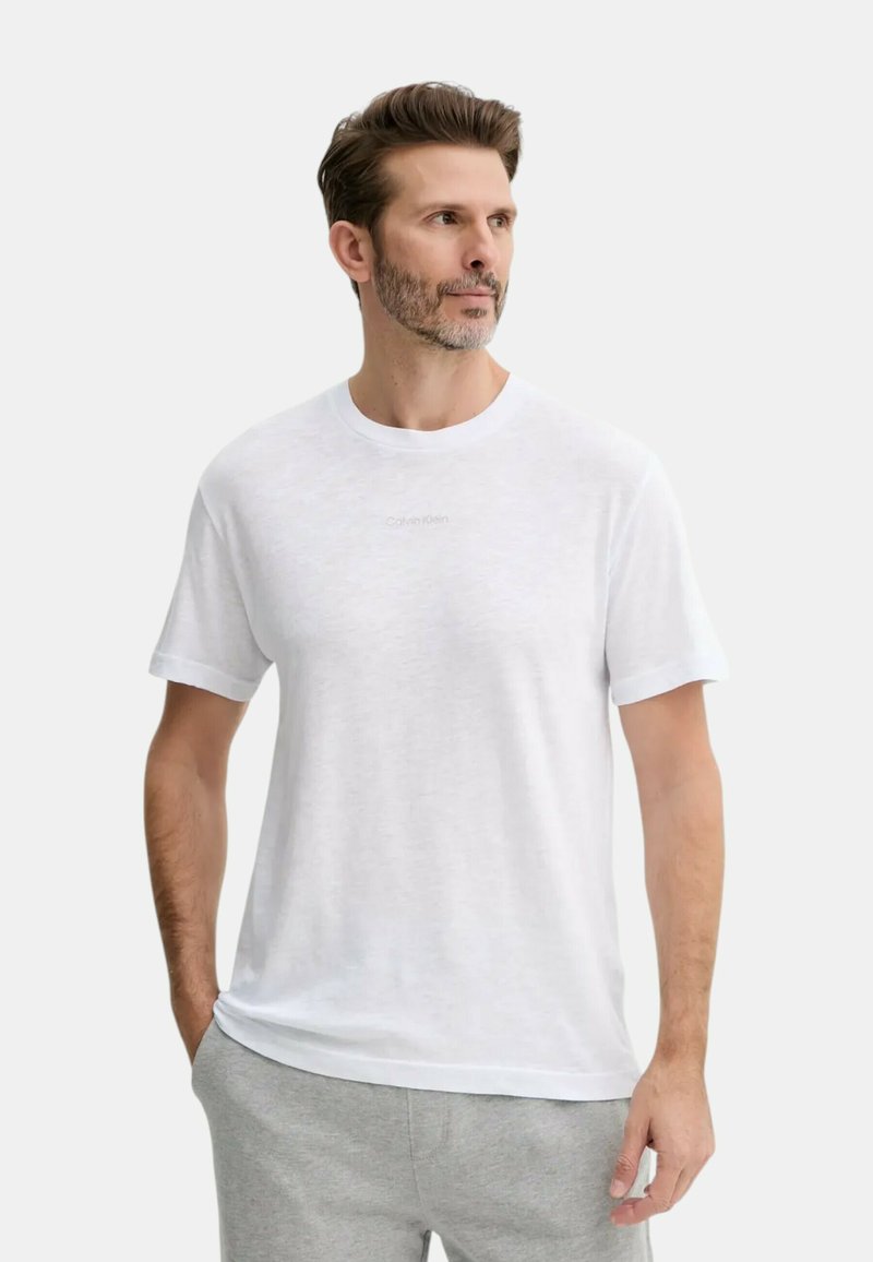 T-shirt bianco in cotone con scollo rotondo e maniche corte; presenta un discreto logo Calvin Klein al centro. Texture morbida e vestibilità rilassata.