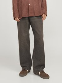 Chemise à carreaux brune avec des manches longues, portée avec un pantalon en denim gris foncé ample et des baskets brunes avec des accents blancs.