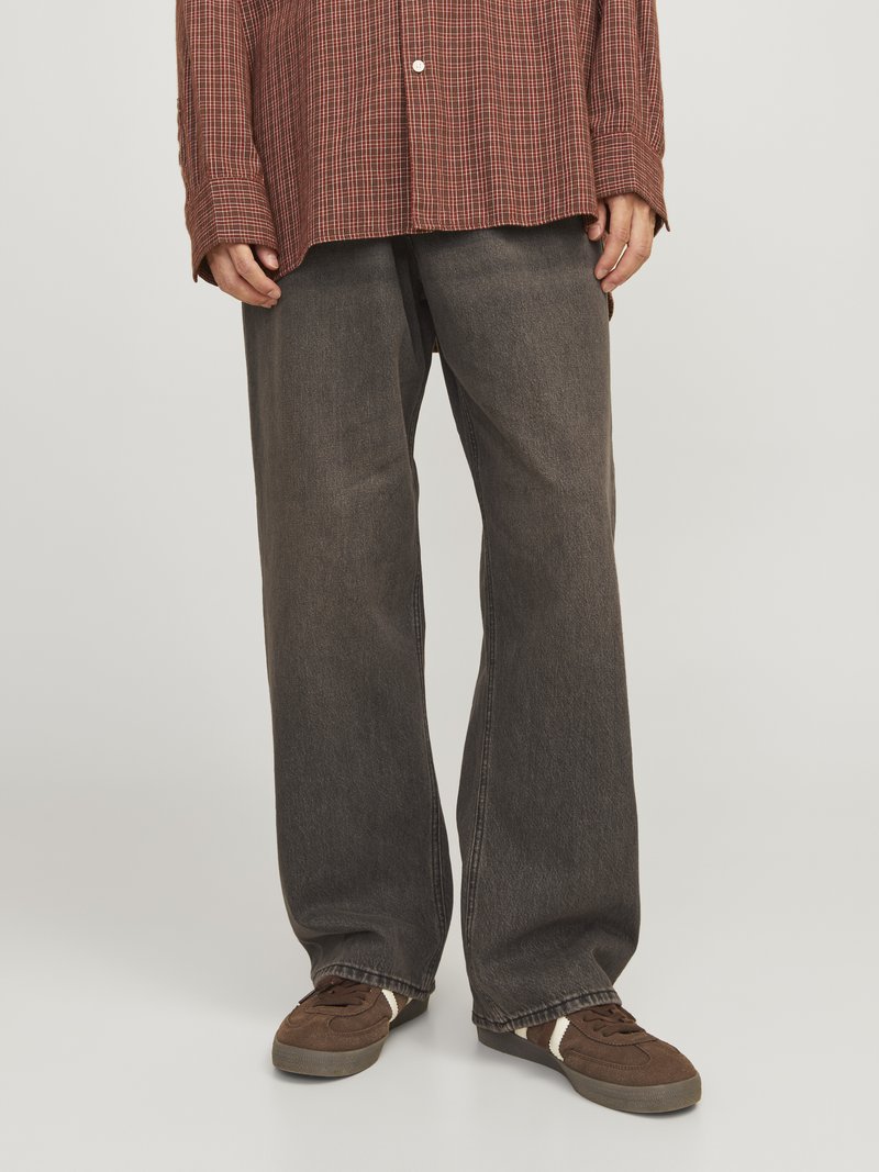 Chemise à carreaux brune avec des manches longues, portée avec un pantalon en denim gris foncé ample et des baskets brunes avec des accents blancs.