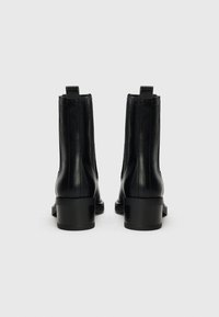 Bottes noires en cuir au niveau de la cheville avec une finition lisse, un bout arrondi, des détails de couture sur les côtés et un petit talon bloc. Tirette à l'arrière.