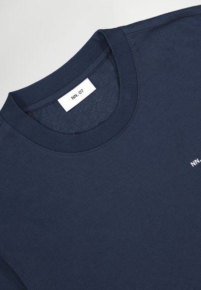 Granatowy T-shirt z dekoltem w łódkę, z prążkowanym kołnierzem i białą metką NN.07 wszytą od wewnątrz przy szyi.