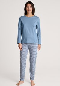 Lichtblauwe langemouwtop gecombineerd met gestreepte pyjamabroek met blauwe en witte geometrische ontwerpen. Zachte katoenen stof, ontspannen pasvorm.