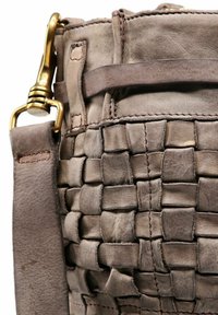 Gros plan sur un sac en cuir taupe avec une texture tissée, des coutures détaillées, une large sangle en cuir et un fermoir en métal doré.