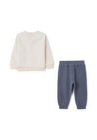 Lichtbeige sweatshirt met ronde hals en knoopsluiting op de rug, gecombineerd met donkerblauwe joggingsbroek met een elastische tailleband.