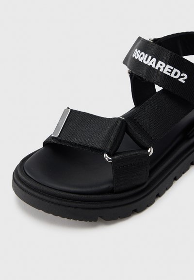 Μαύρα σανδάλια με υφασμάτινα λουριά, φαρδιά ρυθμιζόμενη λωρίδα και παχιά λαστιχένια σόλα με υφή και μεταλλικές λεπτομέρειες.