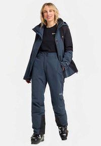 Giacca da sci impermeabile blu navy con cappuccio, pantaloni coordinati e dettagli neri; tessuto liscio e design pratico con logo del marchio visibile.