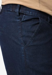 Jeans de mezclilla en azul oscuro con un fit ajustado. Las características incluyen bolsillos clásicos y un sutil detalle de costura a lo largo de las costuras. Textura suave.