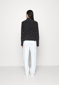 Blusa preta com padrões de folhas coloridas, mangas longas e um corte descontraído, combinada com calças largas brancas.