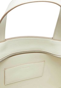 Interno di una borsa in pelle color crema con un compartimento con cerniera. Presenta una texture liscia e una piccola etichetta in rilievo.