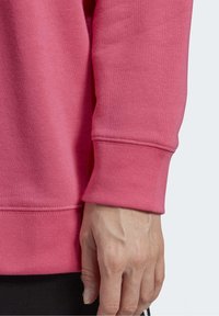 Skräddarsydd rosa sweatshirtärm med ribbad mudd och en slät textur, med en hand som vilar mot den.