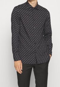 Czarna koszula na guziki z ukośnym białym wzorem. Wykonana z gładkiej tkaniny, z klasycznym kołnierzykiem i długimi rękawami.