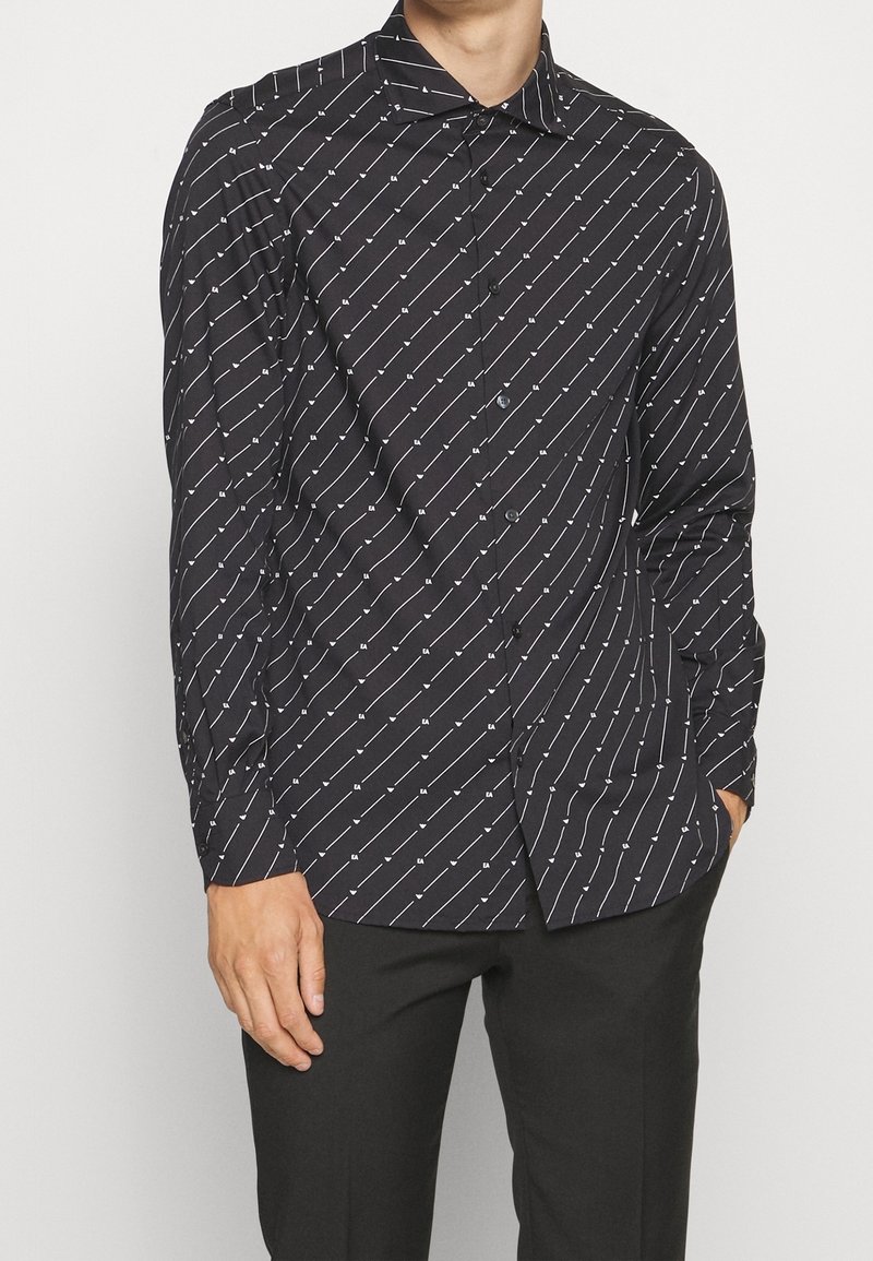 Czarna koszula na guziki z ukośnym białym wzorem. Wykonana z gładkiej tkaniny, z klasycznym kołnierzykiem i długimi rękawami.