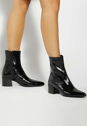 Black patent ankle boots with a pointed toe and block heel. Features a side zipper and a sleek, smooth texture.