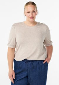 Beige krátký rukáv top s kulatým výstřihem a nařasenými rukávy, zdobený dekorativními knoflíky na rameni, v kombinaci s tmavě modrými kalhotami na šňůrku.