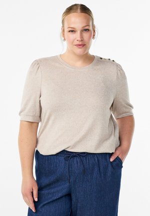 Beige Kurzarmoberteil mit Rundhalsausschnitt und gepufften Ärmeln, mit dekorativen Knöpfen an der Schulter, kombiniert mit dunkelblauen Jogginghosen mit Kordelzug.