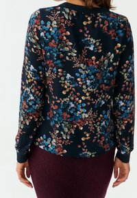 Kwiatowa bluzka z długim rękawem na granatowym tle; posiada kolorowe wzory liści i gałęzi, miękka tkanina oraz okrągły dekolt.