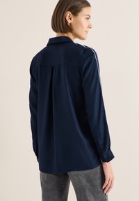 Camicia a maniche lunghe blu navy con colletto, caratterizzata da un taglio dritto, polsini con bottoni e sottili righe bianche lungo le spalle.