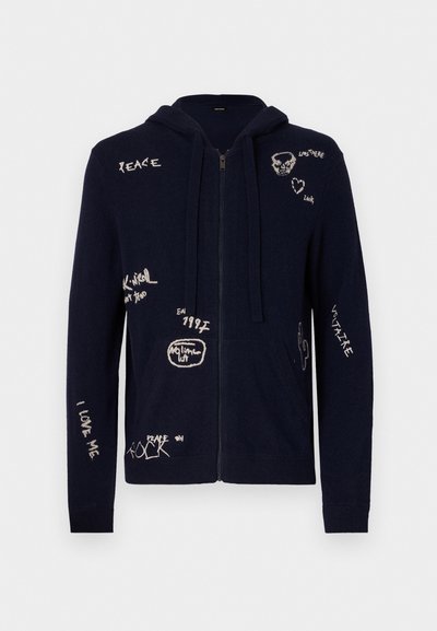 Sweat-shirt zippé bleu marine en tissu doux, comportant divers messages et motifs brodés, y compris des accents de crâne et de cactus.