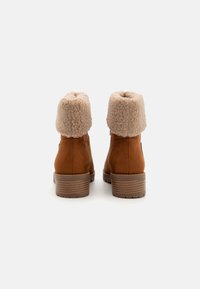 Bottines en suède marron avec un revers en fausse fourrure beige, talon empilé et intérieur rembourré pour le confort.
