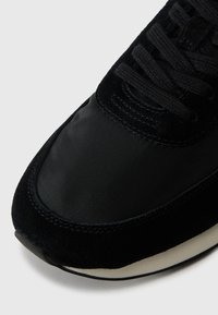 Zwarte sportschoen met een bovenwerk van suede en nylon, een afgeronde neus, een gestructureerd oppervlak en veters met bijpassende zwarte veters voor een stevige pasvorm.