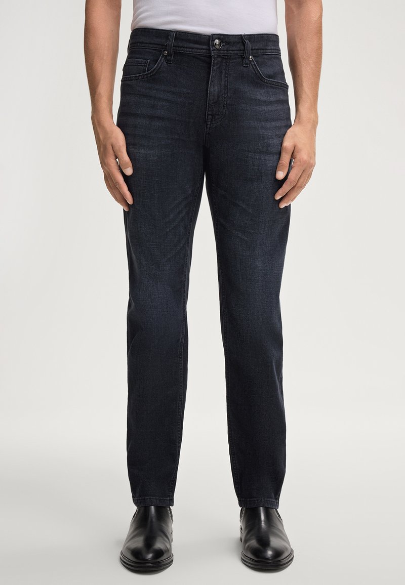 Jean en denim bleu foncé avec une coupe droite, cinq poches et un bouton de fermeture. Le tissu semble lisse avec un minimum de décoloration.