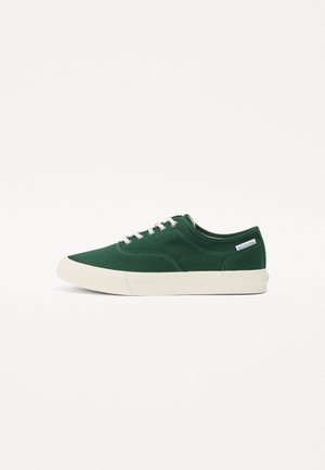 Zielony niski sneaker z płótna z białymi sznurówkami i podeszwą, z małą białą metką z logo Hilfiger blisko pięty.