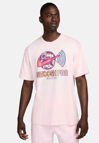 Camiseta de algodón rosa claro con un diseño gráfico de un globo terráqueo y ondas sonoras, con el texto "SWOOSH FUN" en colores vibrantes. Manga corta, corte relajado.